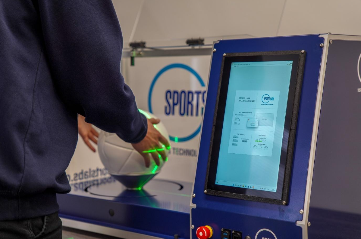 Sports Labs Ball Balance Test Device measuring a white football with green laser alignment grid and live data screen.