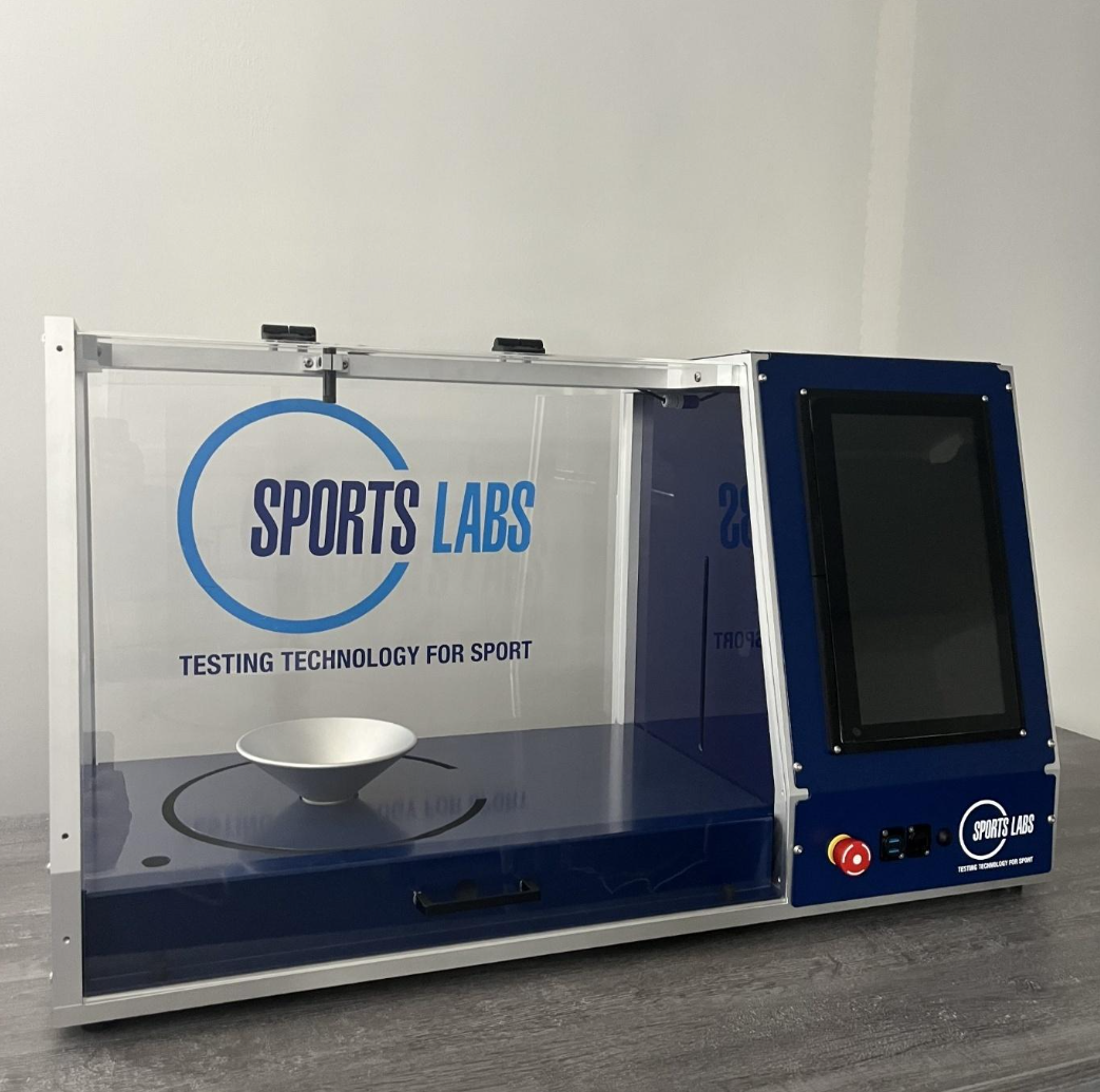 The Sports Labs Balance Test Device shown empty, with branded acrylic enclosure, integrated touchscreen display, and ball cradle visible.